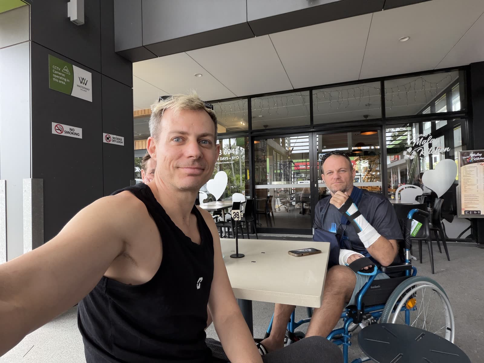 Ben and his brother Kris at a cafe. Kris is in a wheelchair with both arms in casts and braces.